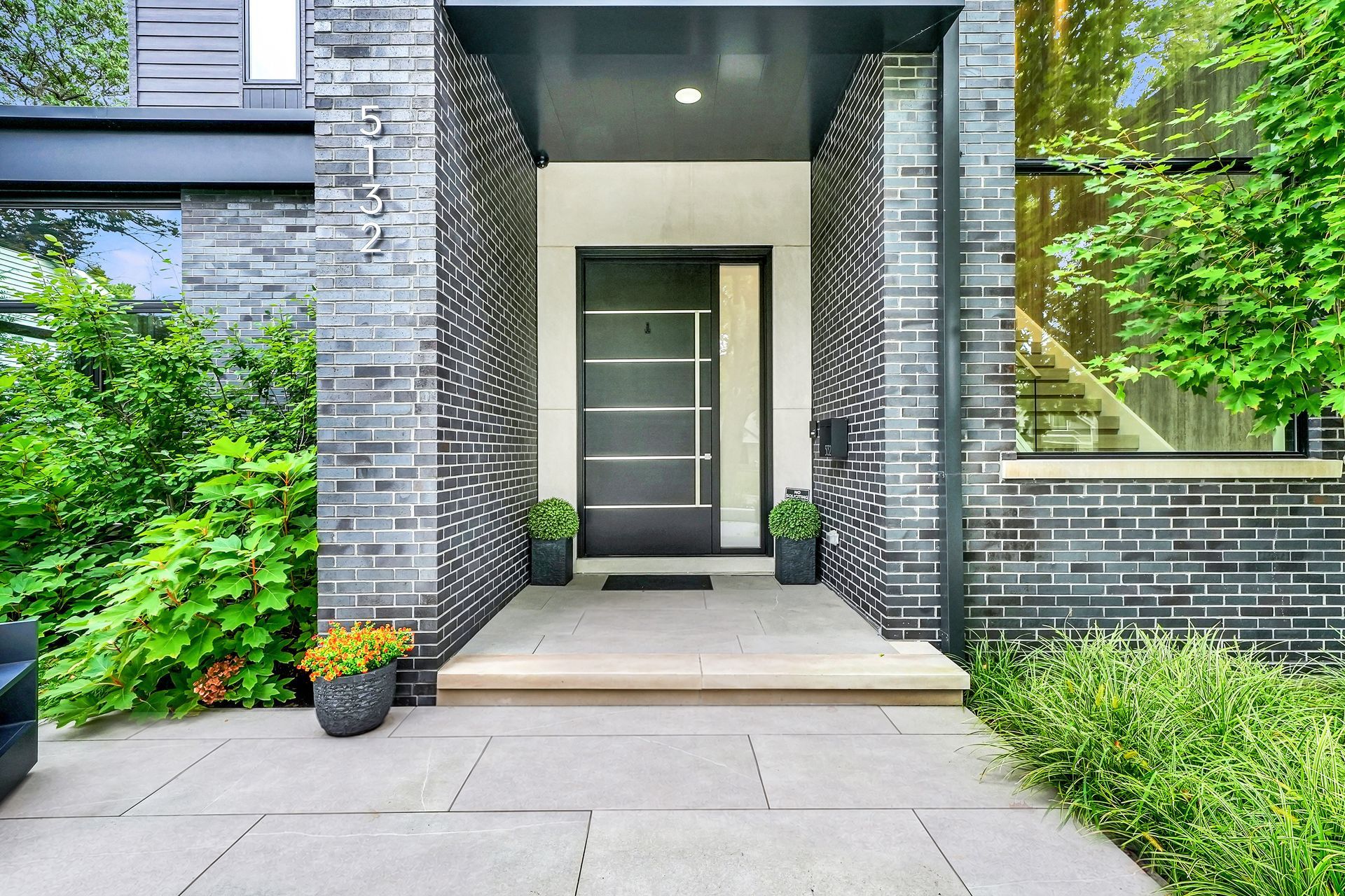 Modern home entrance with gray brick walls, glass door, and greenery along a front walkway