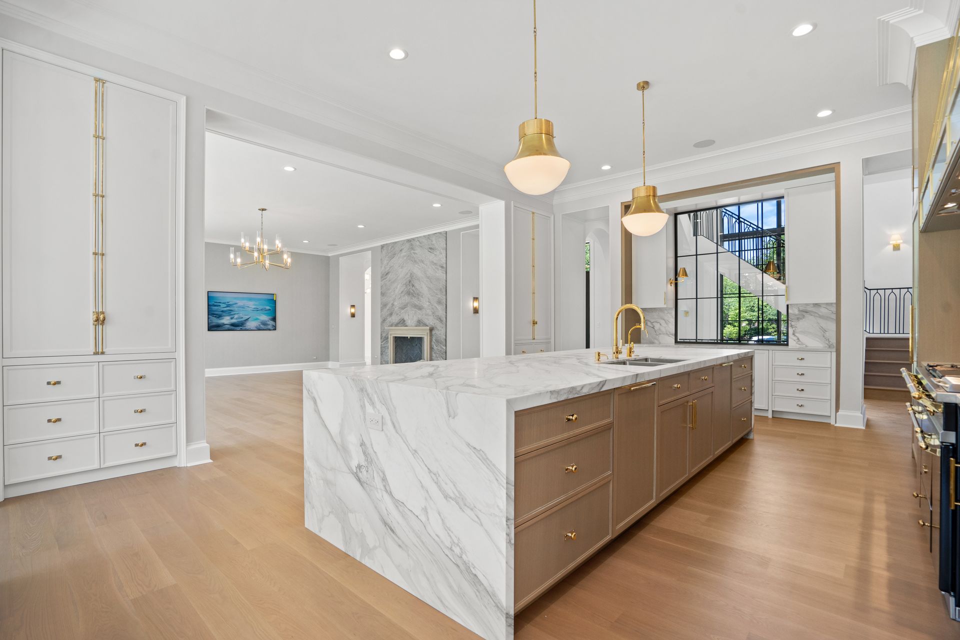 Bright modern kitchen with marble island, white cabinets, wood floors, and gold pendant lights