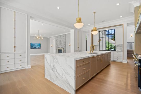 Bright modern kitchen with marble island, wood floors, gold pendant lights, and large windows