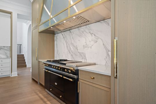 Luxury kitchen with black stove, gold accents, marble backsplash, and light wood cabinets