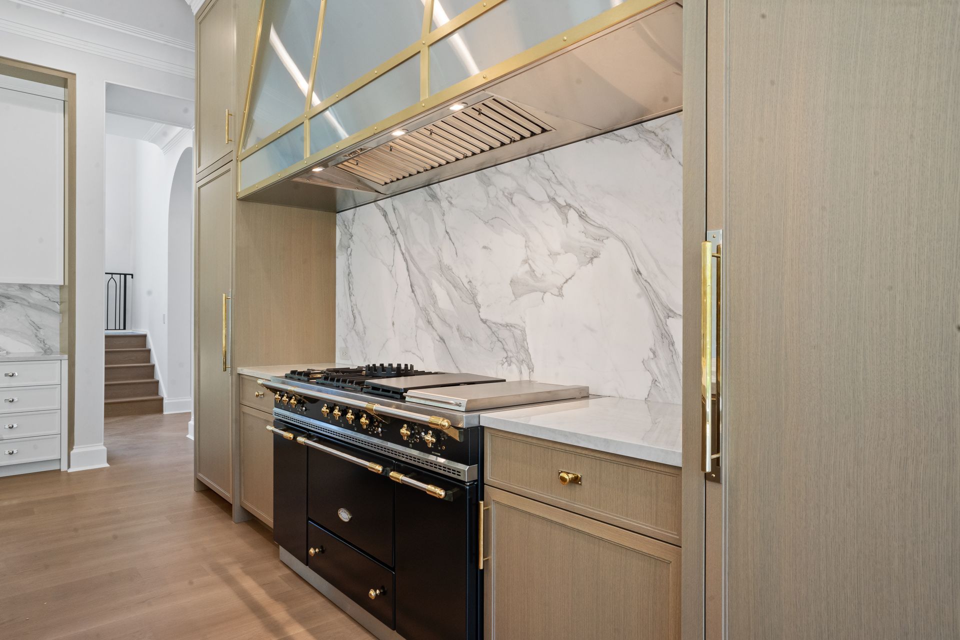 Modern kitchen with black stove, gold accents, and marble backsplash beside a light wood island