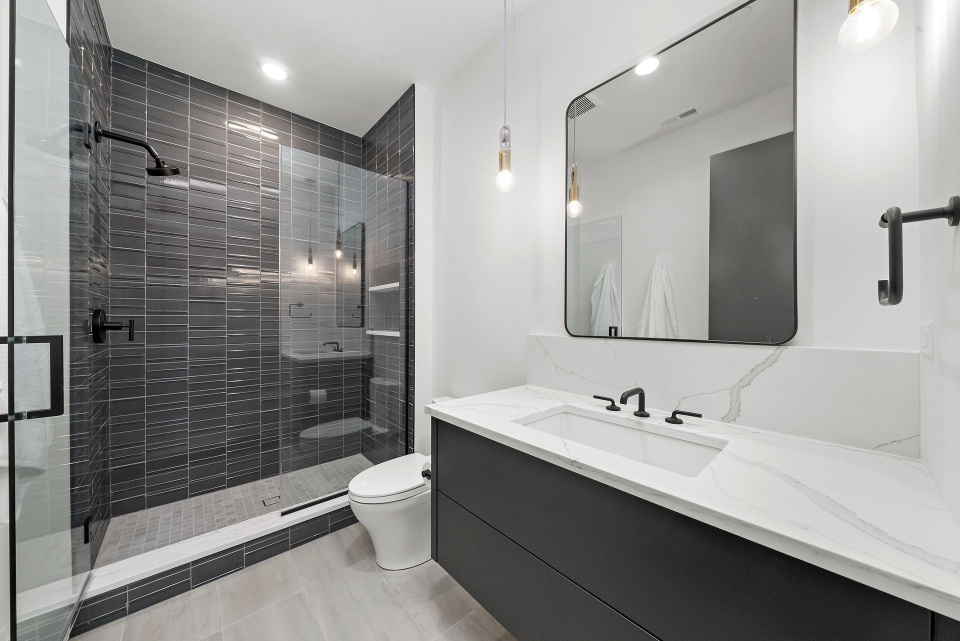 Modern bathroom with black-tiled shower, white vanity, large mirror, and toilet