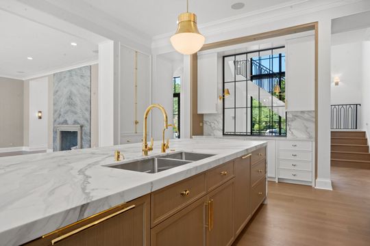 Bright modern kitchen with marble island, gold faucet, and staircase beside a window