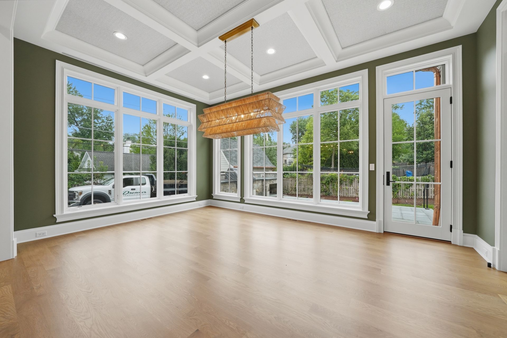 Bright empty sunroom with large windows, light wood floor, gray walls, and a woven hanging light fixture.