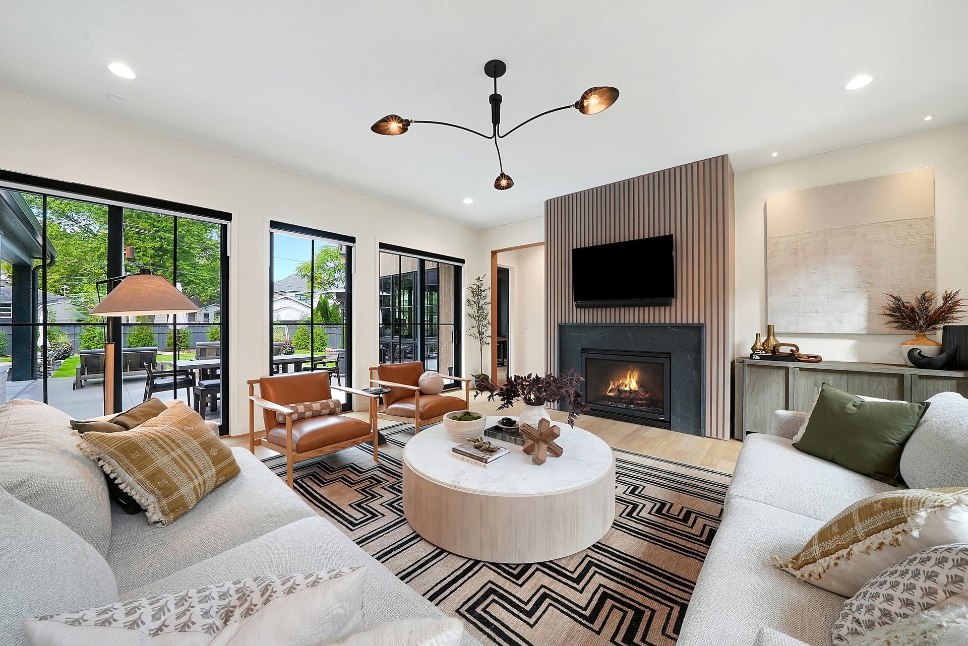Bright modern living room with fireplace, large windows, sectional sofas, round coffee table, and patterned rug