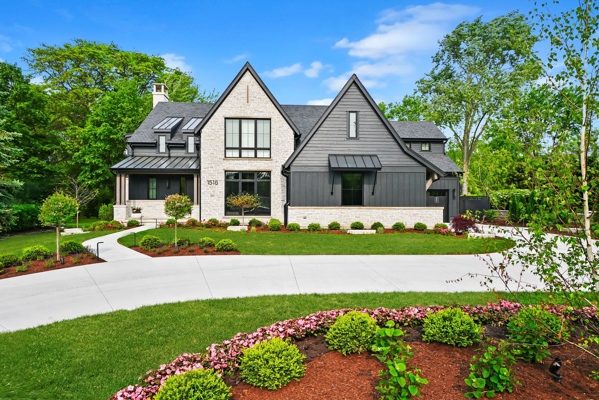 Modern gray house with gabled roof, curved driveway, and landscaped front yard under a bright blue sky