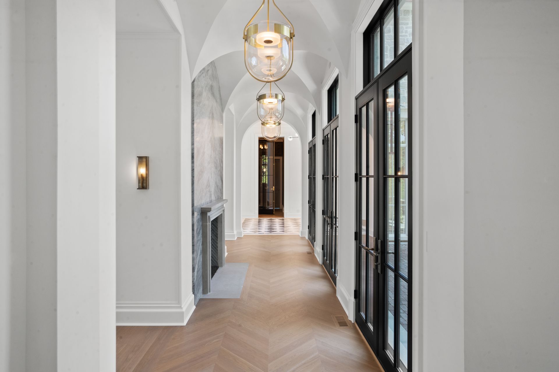 Bright hallway with arched ceiling, pendant lights, herringbone floor, and black-framed glass doors.