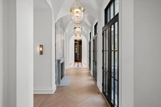 Bright hallway with arched ceilings, pendant lights, and black-framed glass doors.