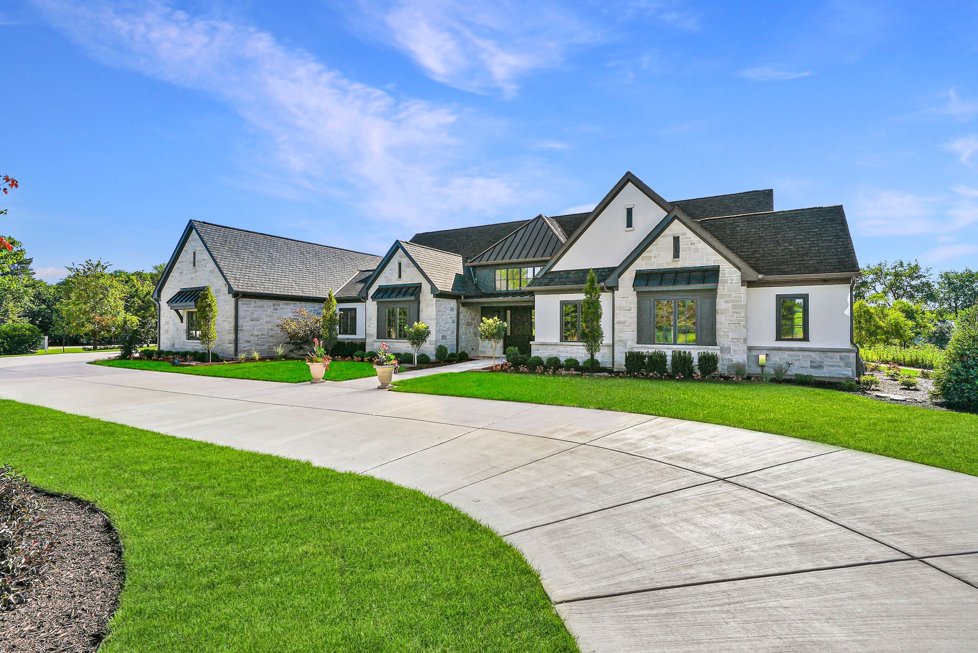 Large white suburban house with a curved driveway, green lawn, and bright blue sky