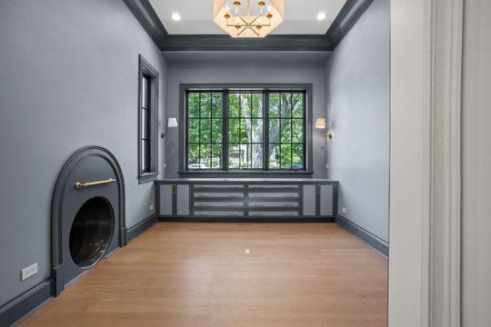 Empty modern room with gray walls, hardwood floor, built-in window bench, and black fireplace surround
