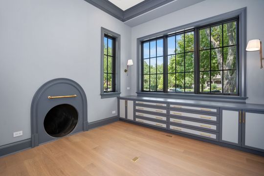 Bright empty room with gray walls, large windows, built-in radiator cover, and a fireplace opening