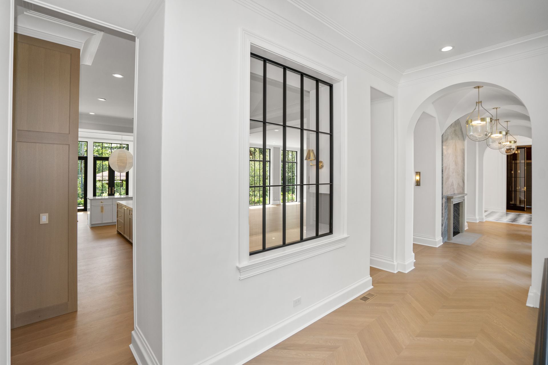 Bright white hallway with herringbone wood floors, arched doorway, and black-framed window indoors