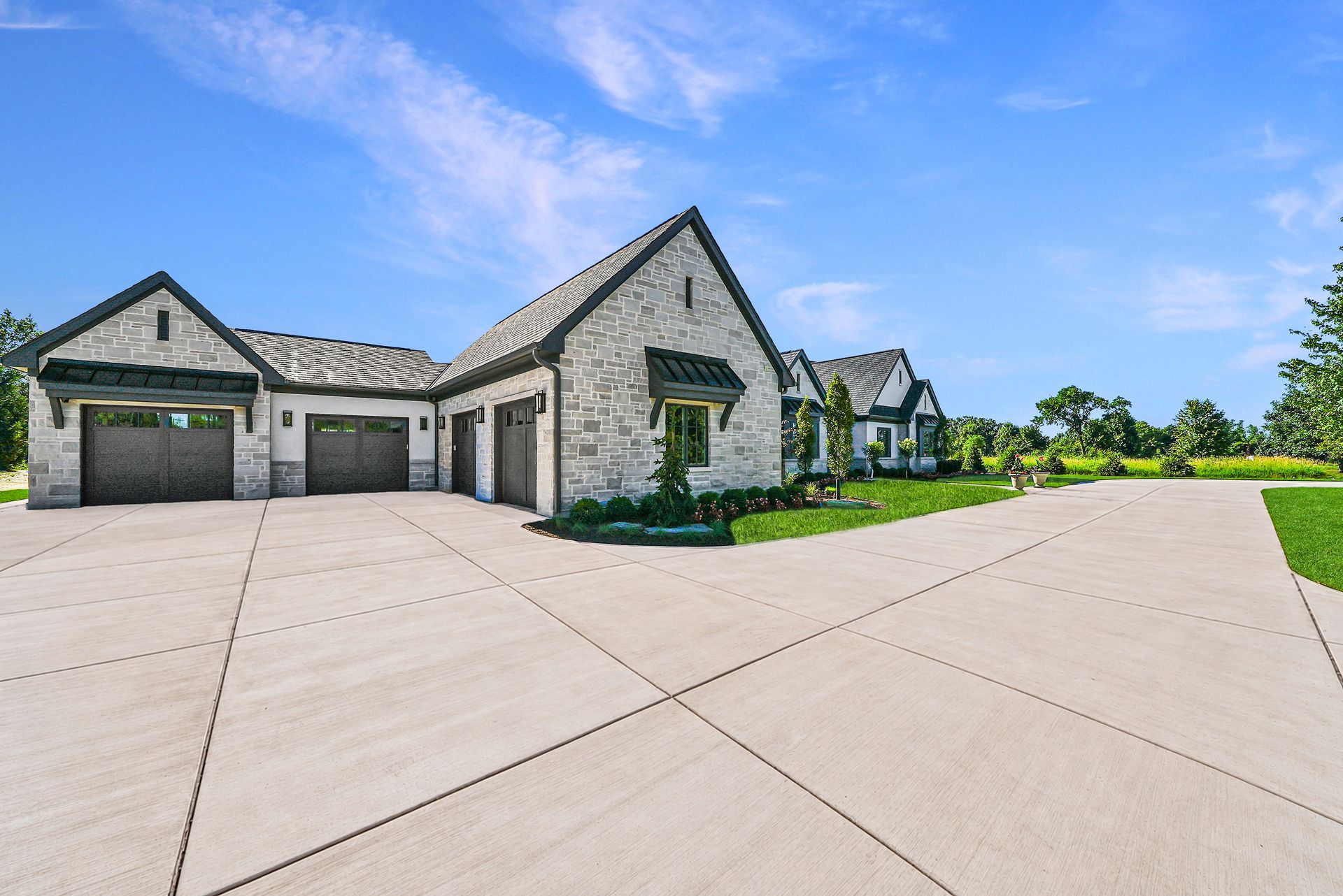 Modern stone suburban house with three garage doors, a wide concrete driveway, and a blue sky.