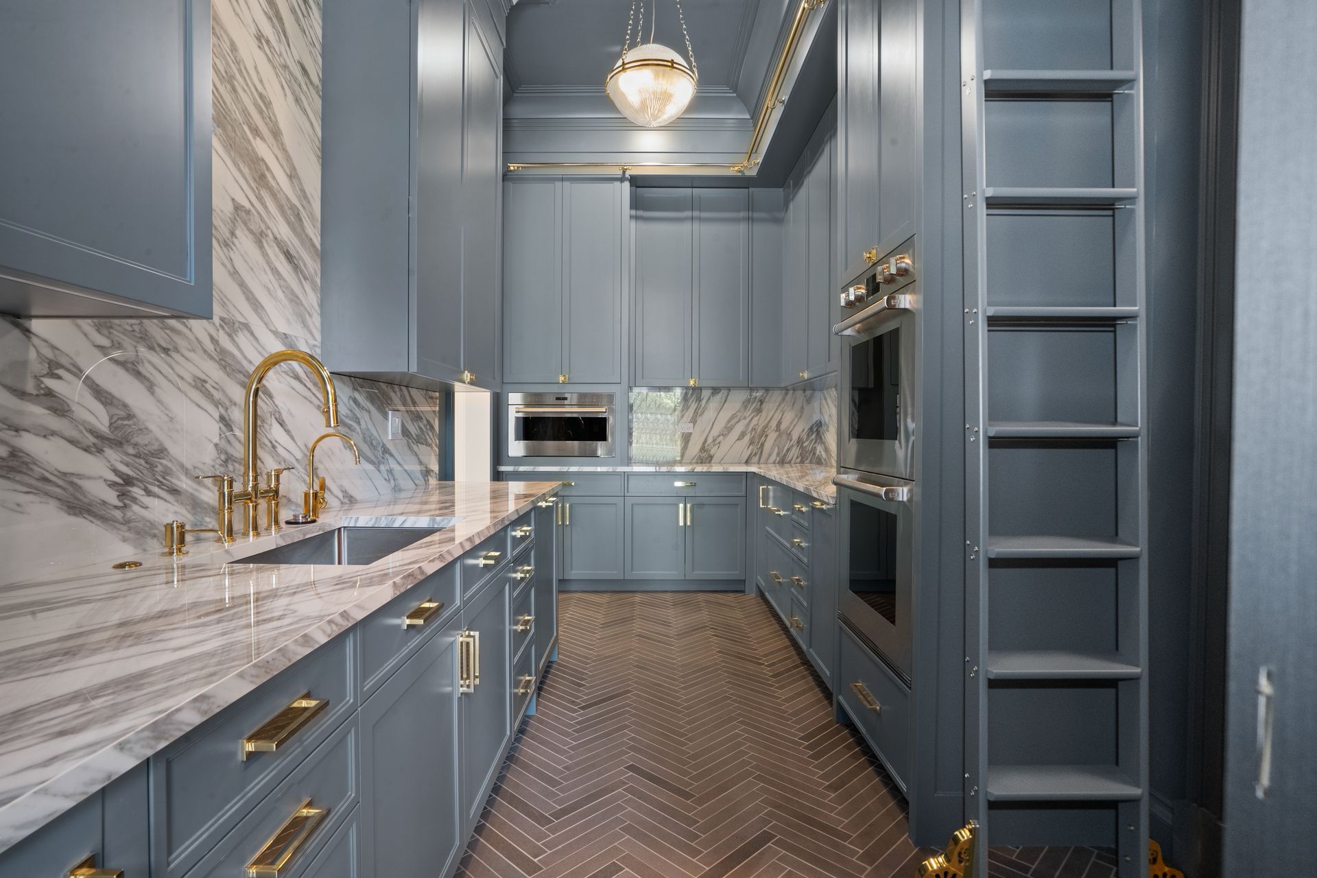 Narrow blue galley kitchen with marble countertops, gold faucet, and built-in appliances