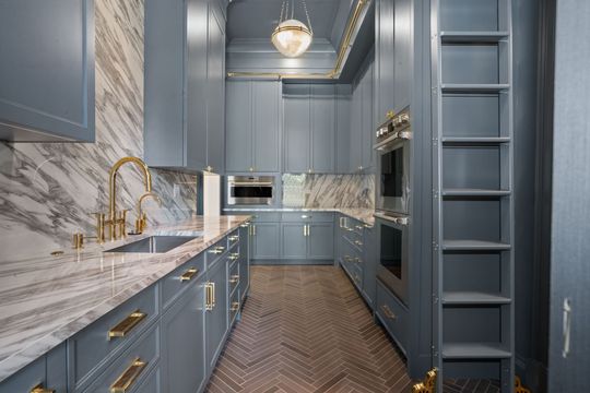 Narrow blue kitchen with marble counters, gold fixtures, and built-in appliances in a modern hallway layout