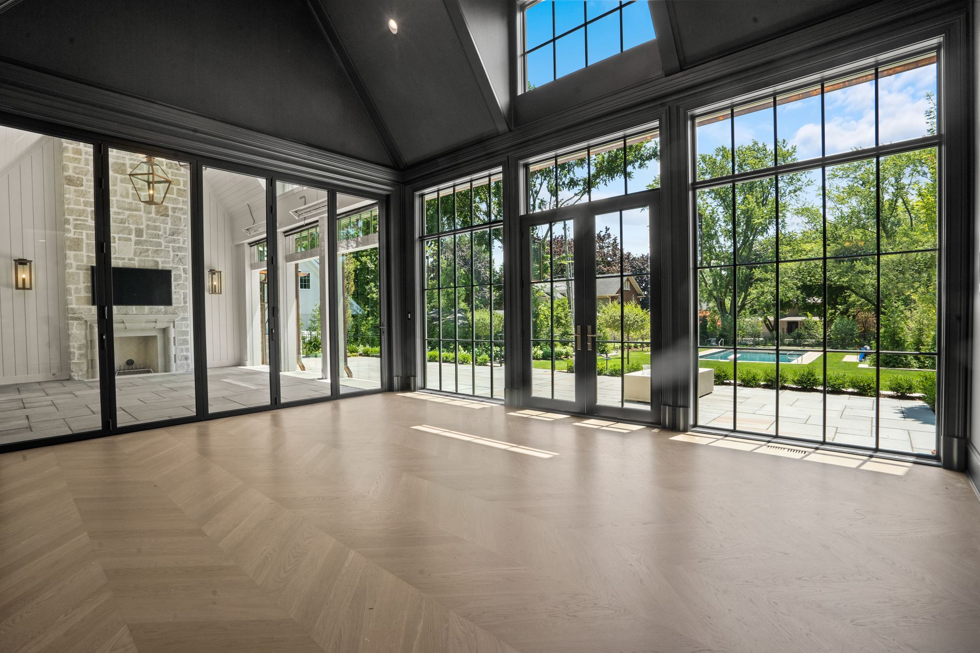Empty modern room with large black-framed windows and sunlight on a light wood floor