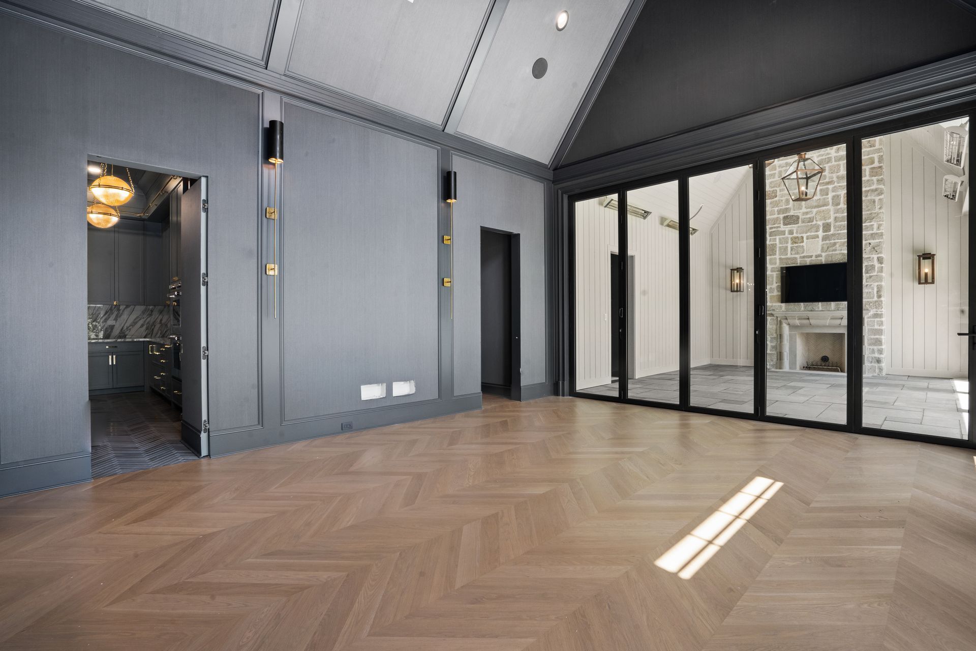Empty modern room with gray walls, herringbone wood floor, and large black-framed glass doors to the terrace