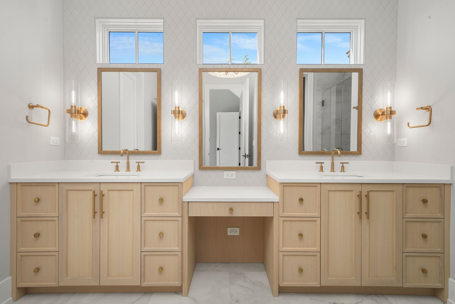 Bright double vanity bathroom with light wood cabinets, three mirrors, and brass wall sconces