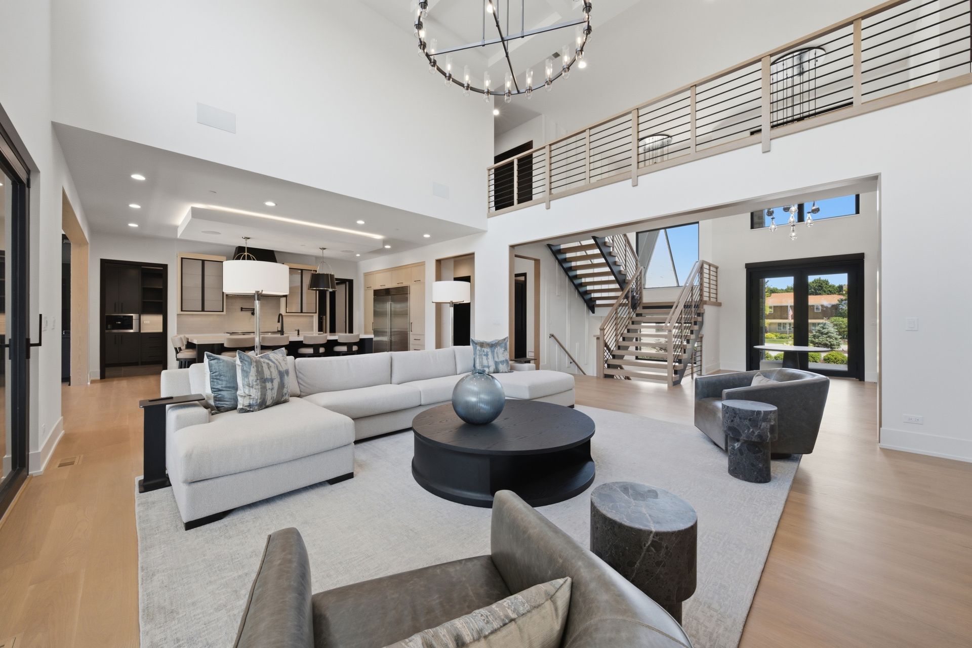 Modern open-plan living room with gray sectional, loft railing, staircase, and kitchen beyond