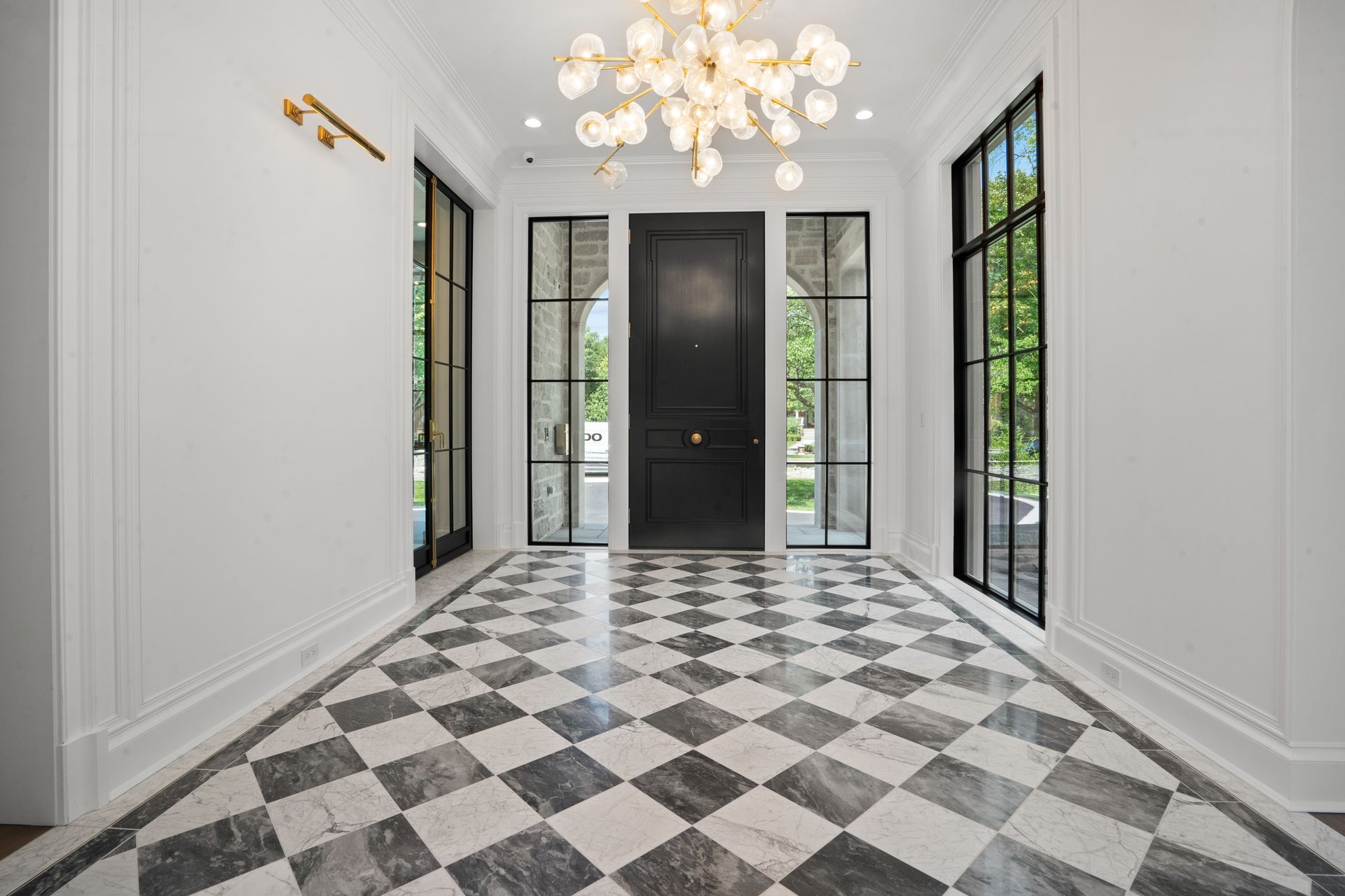Elegant foyer with black-and-white checkered floor, chandelier, and glass doors leading outside
