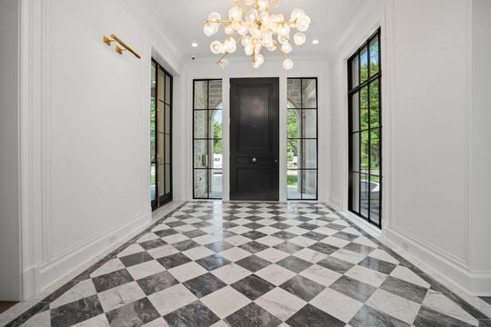 Elegant foyer with black-and-white checkered floor, white walls, chandeliers, and a black front door.