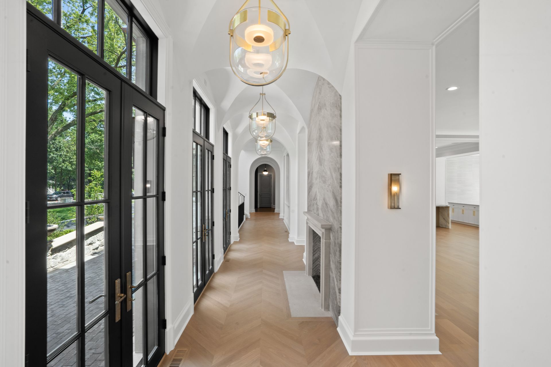 Bright hallway with arched black-framed windows, pendant lights, and herringbone wood floors