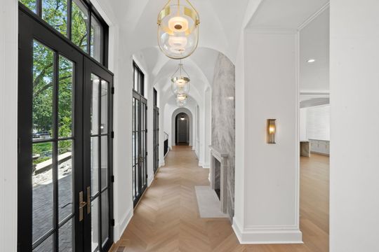 Bright hallway with black-framed windows, white walls, pendant lights, and herringbone wood floor.