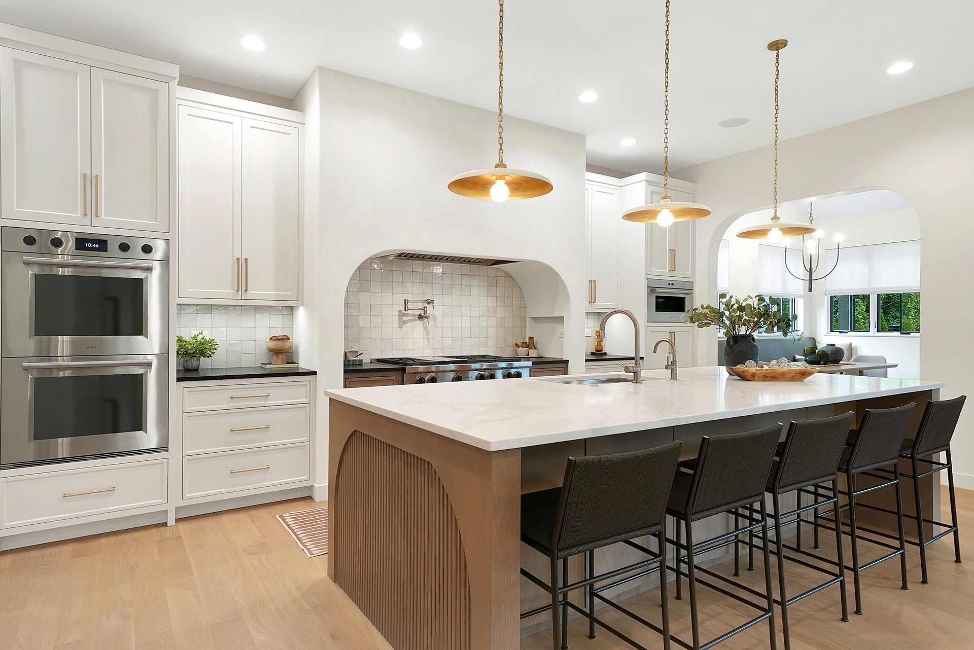 Bright modern kitchen with white cabinets, marble island, pendant lights, and black barstools