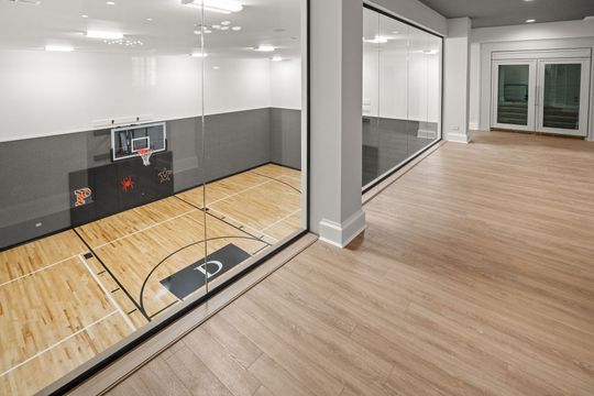 Indoor basketball court with wood floor, glass wall, and open lounge area with large windows