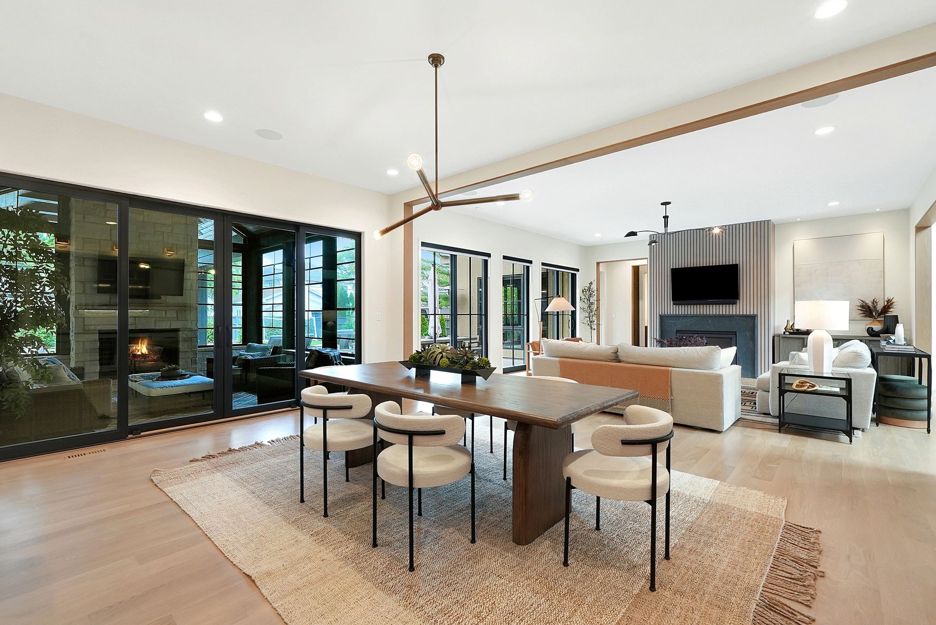 Modern open-plan living and dining room with a large table, beige sofa, fireplace, and floor-to-ceiling windows