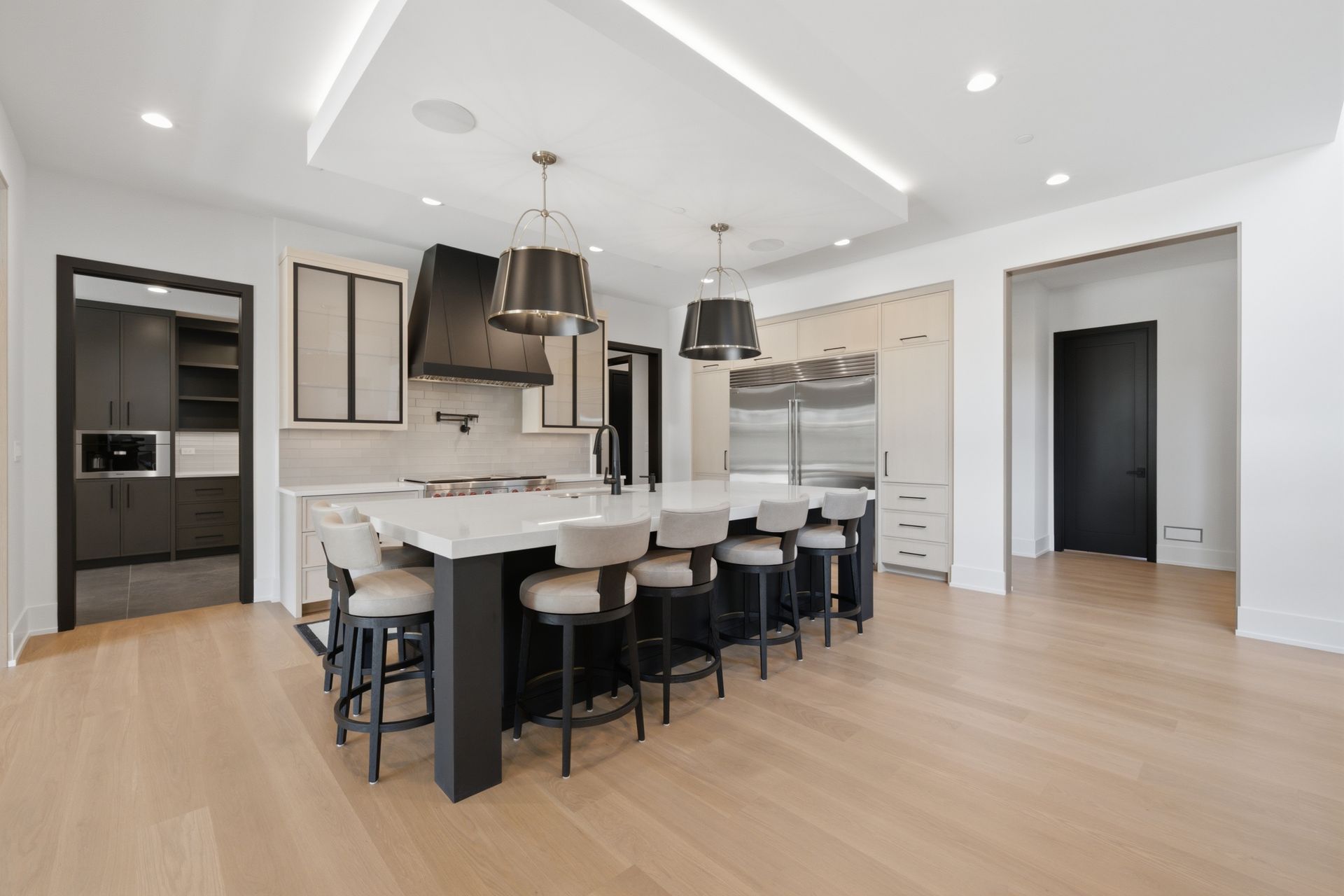 Modern open kitchen with white cabinets, large island, black stools, pendant lights, and light wood floors