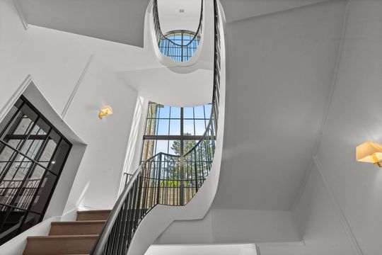 Grand staircase with curved walls, black railings, and a skylight in a bright white interior
