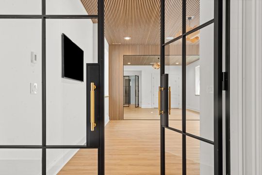 Modern office entry with glass doors, black frames, gold handles, and wood flooring