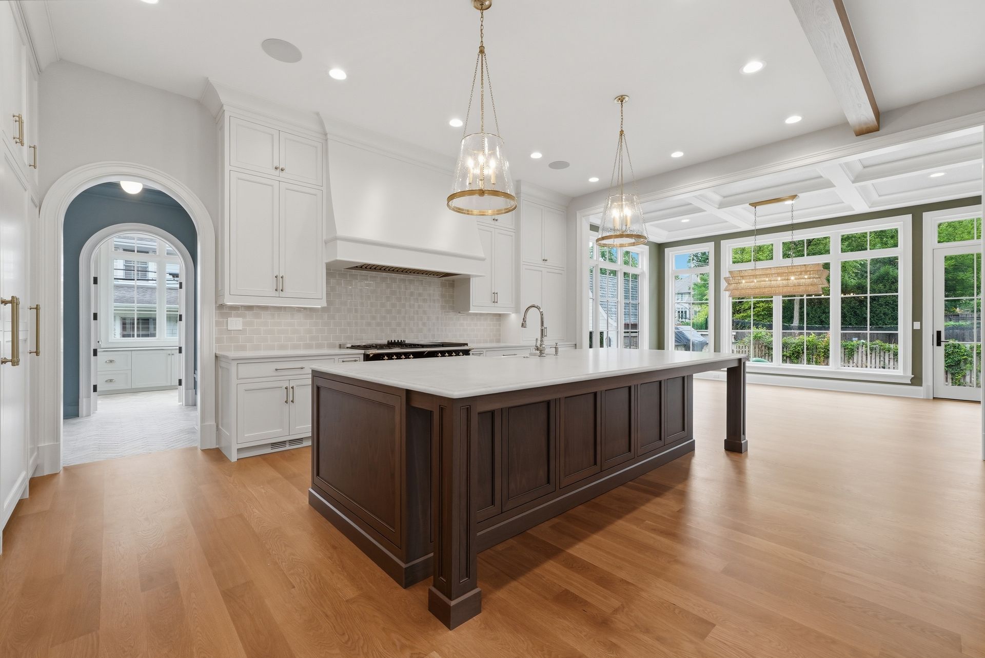 Bright white kitchen with dark wood island, hardwood floors, and large windows overlooking greenery