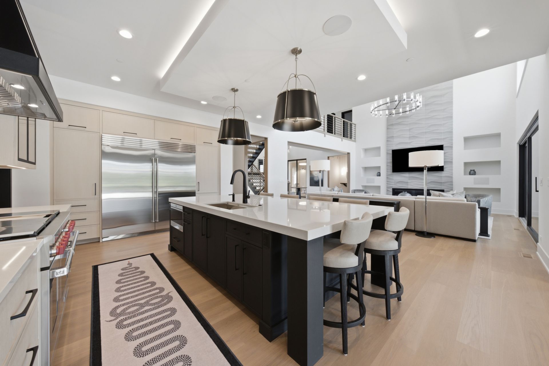 Modern white kitchen with a large dark island, stainless steel appliances, and light wood floors