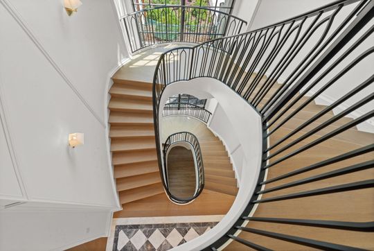 Spiral staircase with wooden steps, white walls, black railing, and patterned tile floor viewed from above