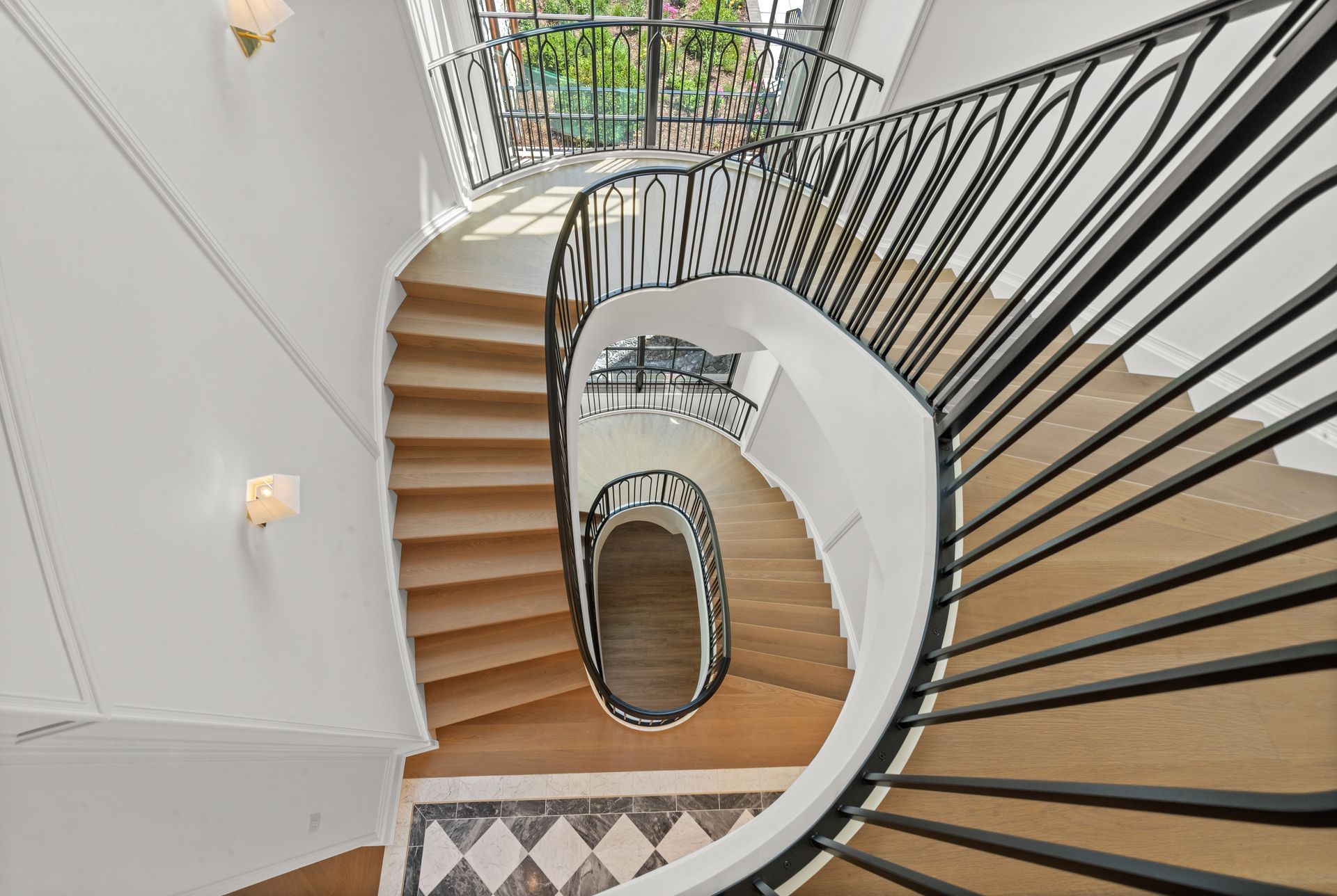 Top-down view of a curving staircase with wood steps, black railings, and patterned tile floor