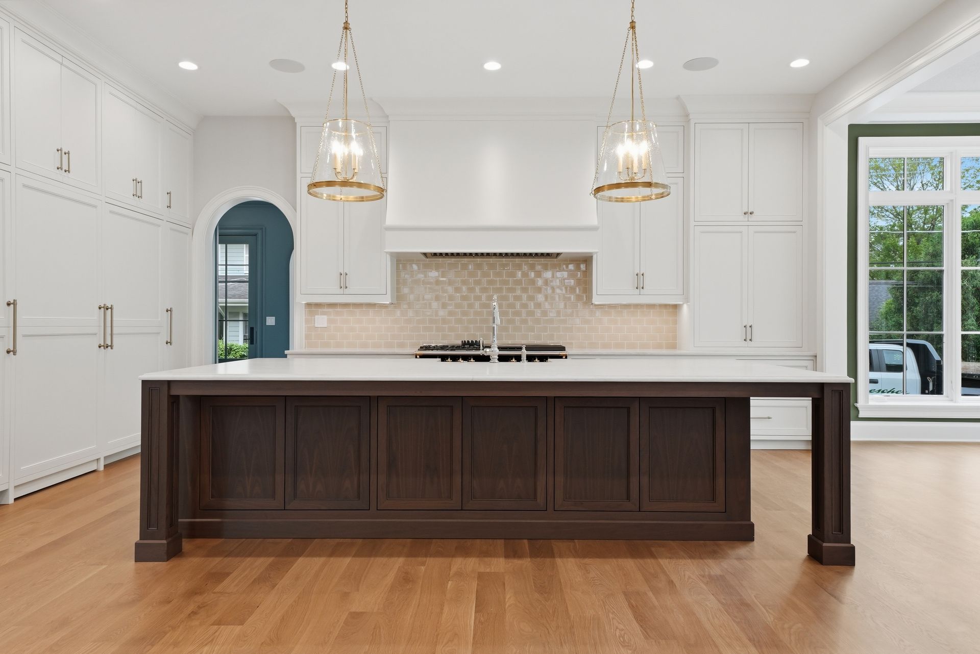 Bright white kitchen with a dark wood island, brass pendants, and a large windowed door.
