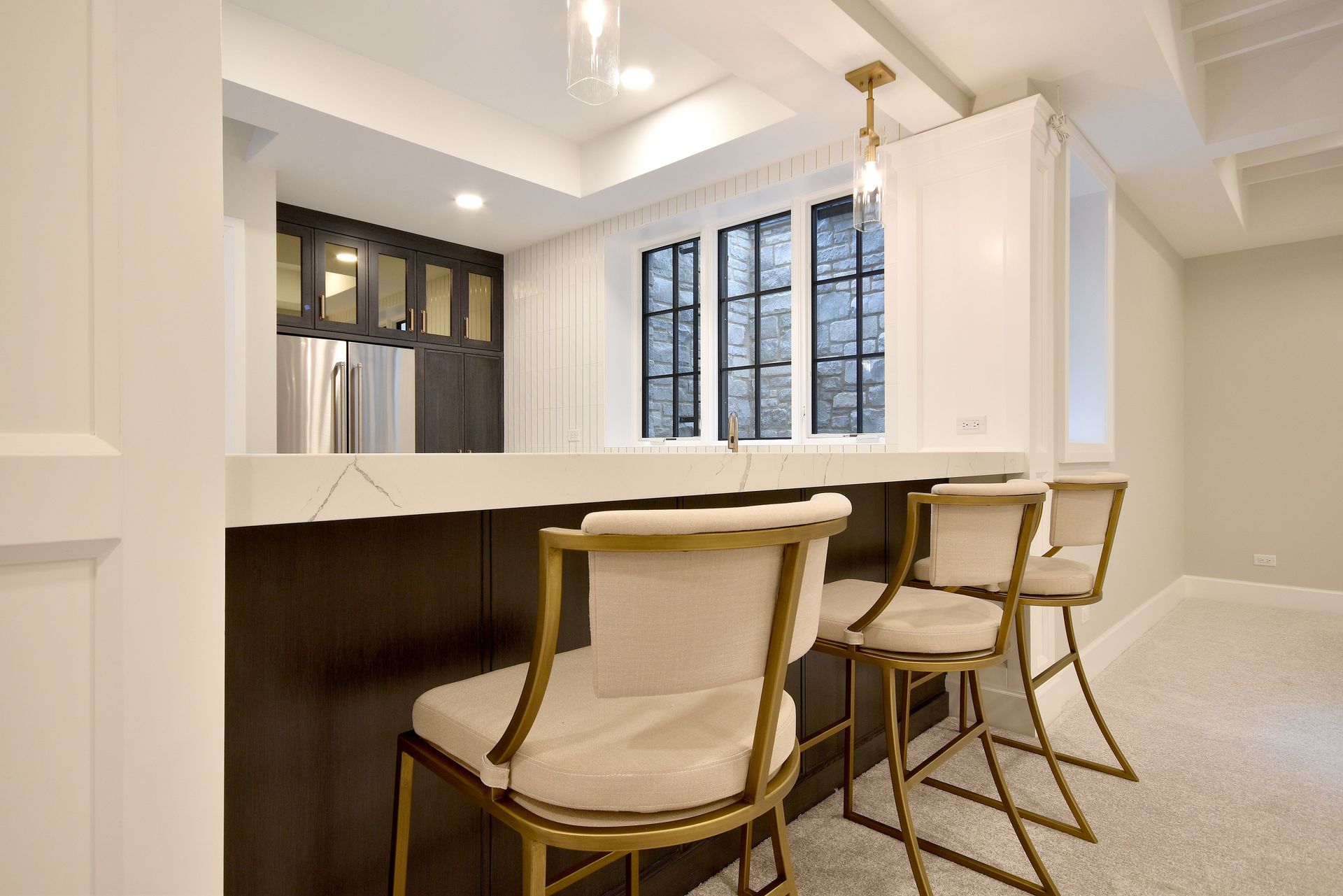 Modern kitchen with white cabinets, dark island, and two gold-framed bar stools in a bright interior