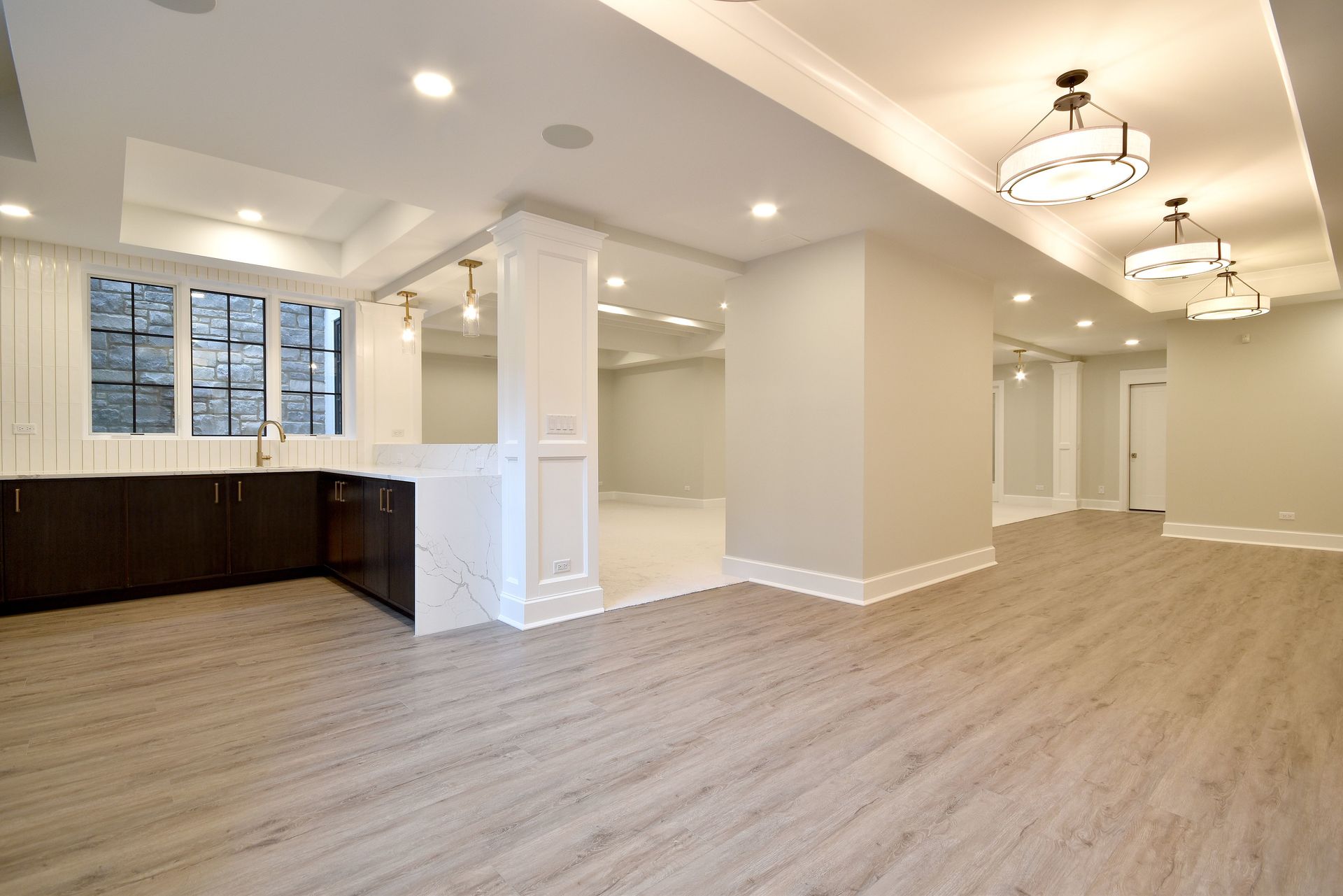 Spacious empty modern living area with hardwood floors, white walls, and a kitchen nook by large windows