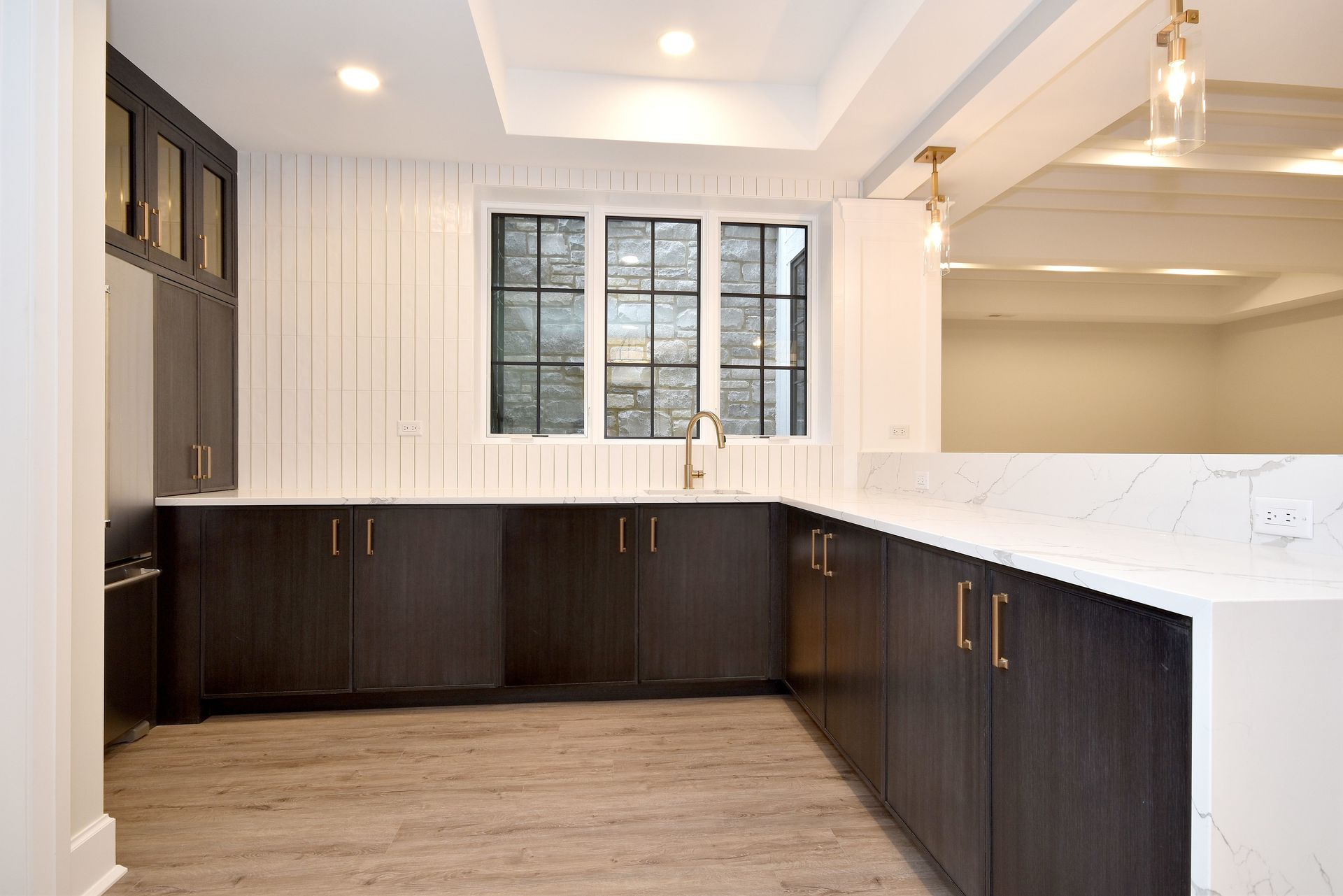 Modern kitchen with dark wood cabinets, white counters, and a central window over the sink