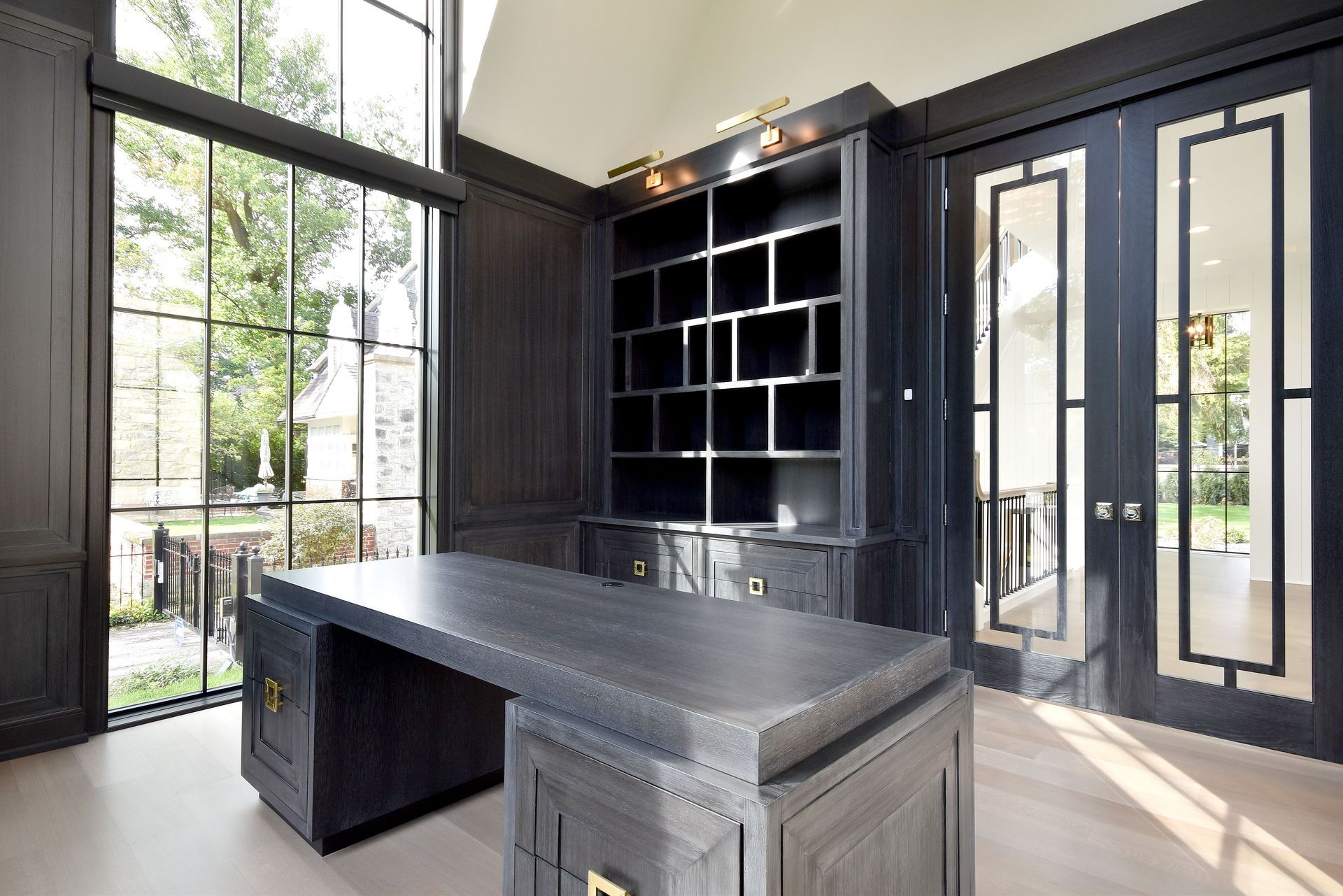 Modern black office with built-in shelves, large windows, and a dark wood desk in the center