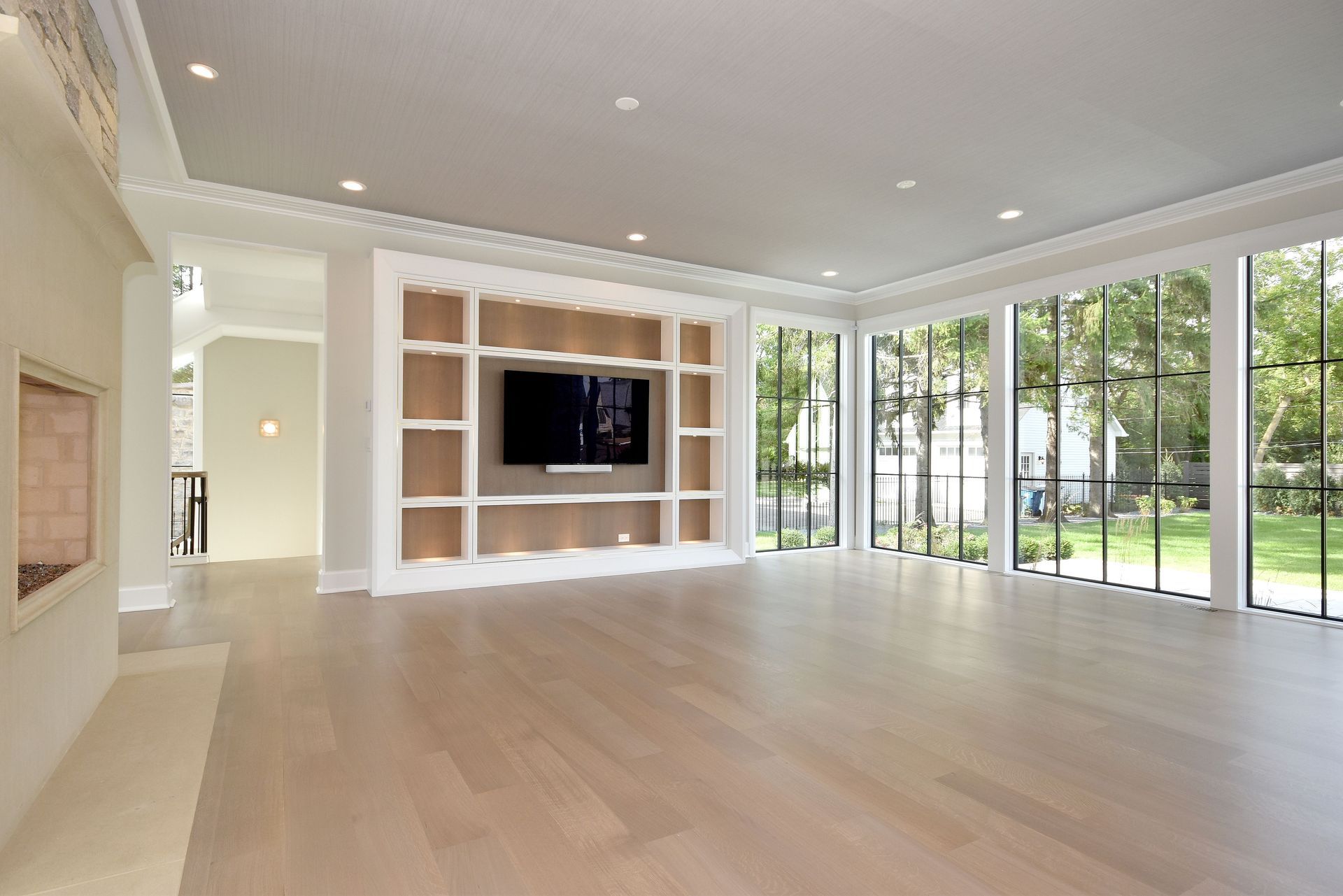 Bright modern living room with built-in TV wall and large floor-to-ceiling windows overlooking greenery