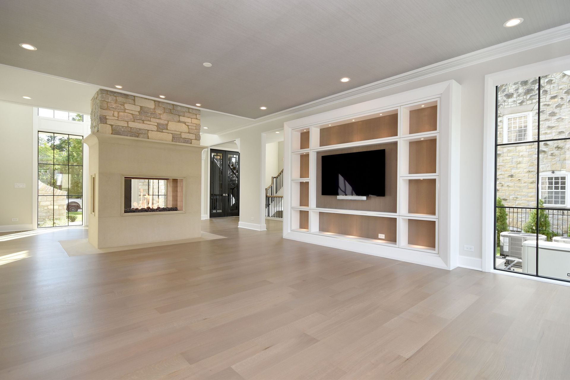 Bright modern living room with light wood floors, stone fireplace, built-in shelves, and a wall-mounted TV.