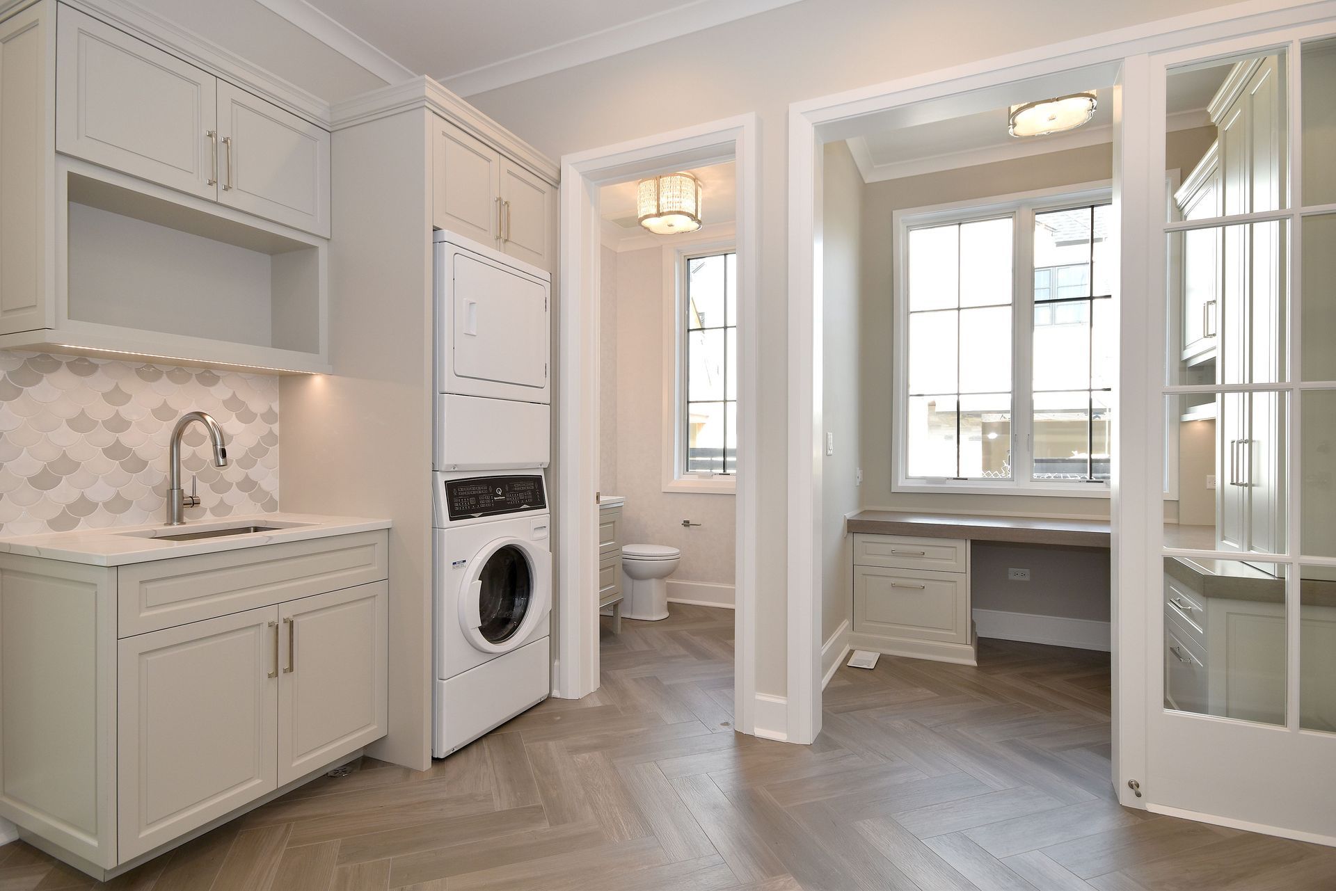 Bright white laundry room with stacked washer-dryer, built-in cabinets, and a desk nook by the window.