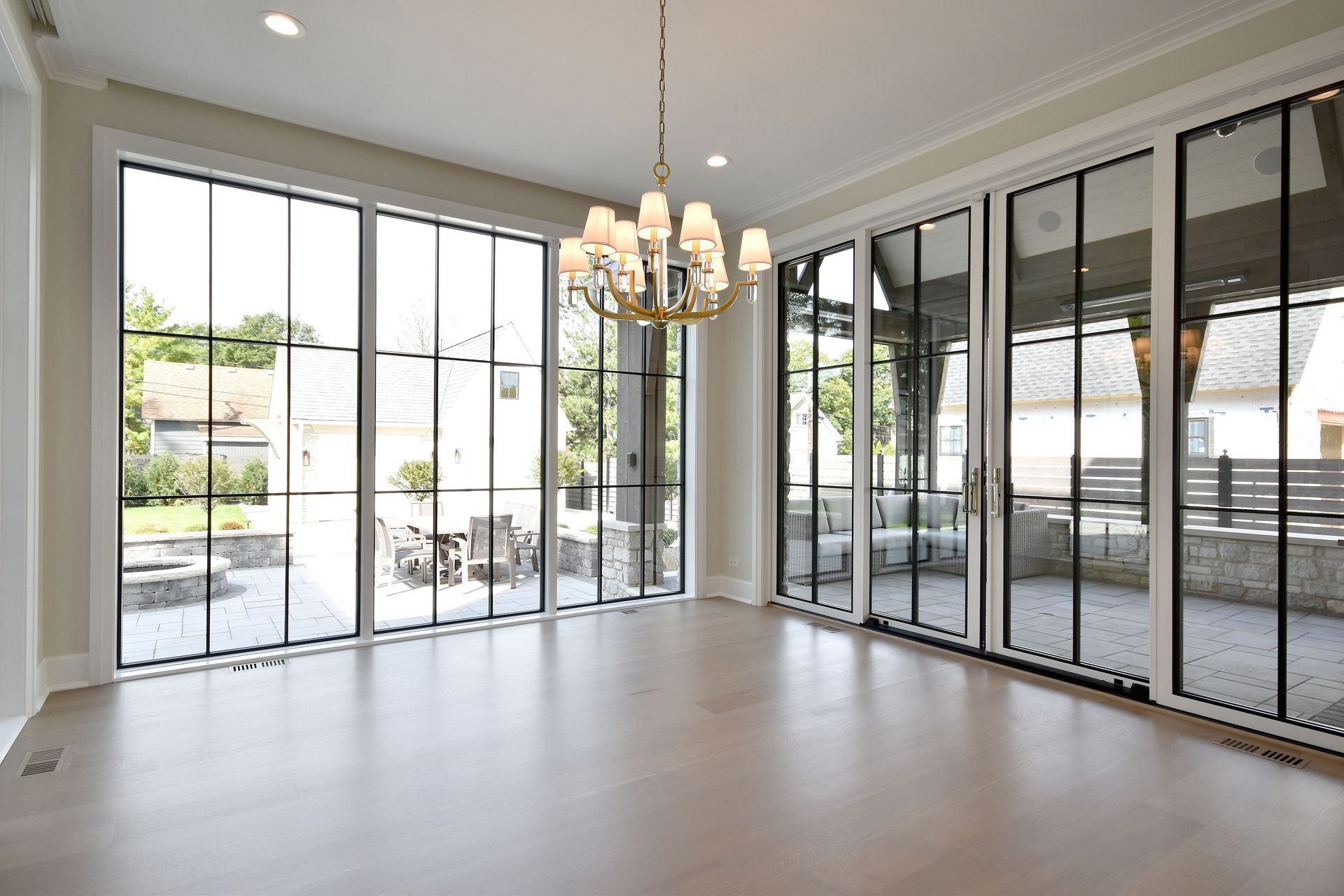 Bright empty room with large windows, glass doors, and a chandelier overlooking a patio