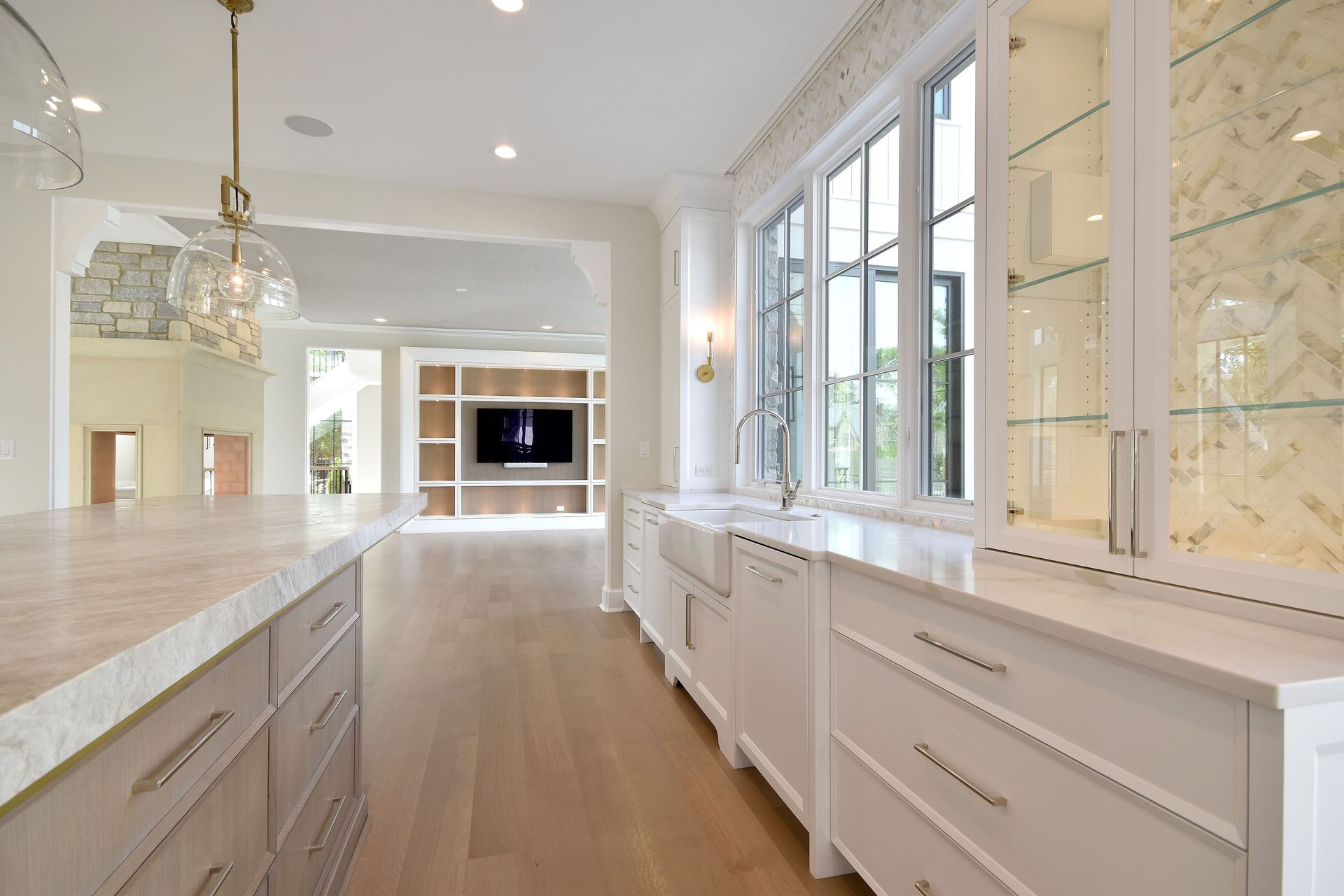 Bright modern kitchen with white cabinets, marble counters, and a large sunlit window.