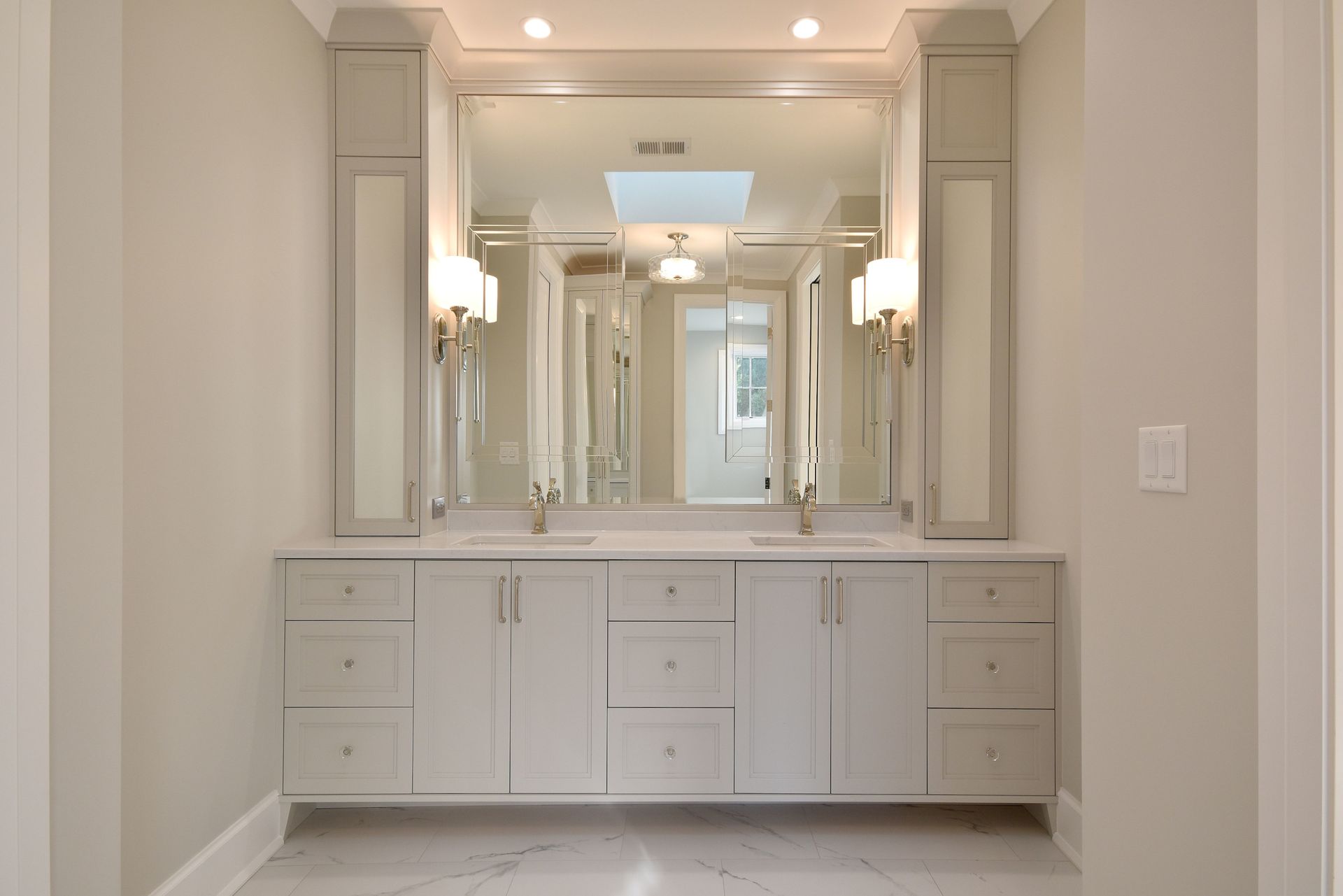 Bright white bathroom vanity with large mirrors, built-in cabinets, and overhead lighting