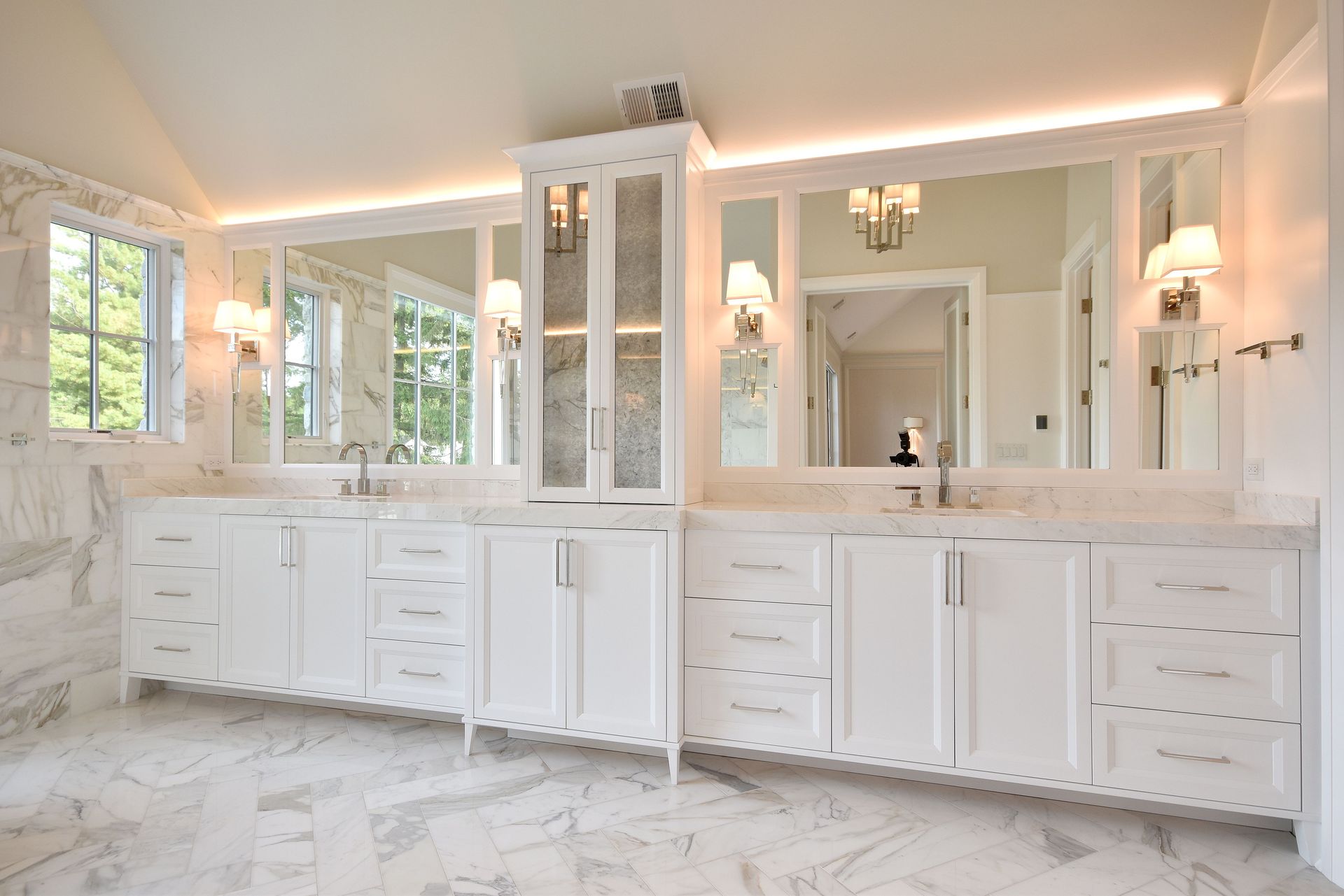 Bright white luxury bathroom with double vanities, mirrors, chandeliers, and large windows