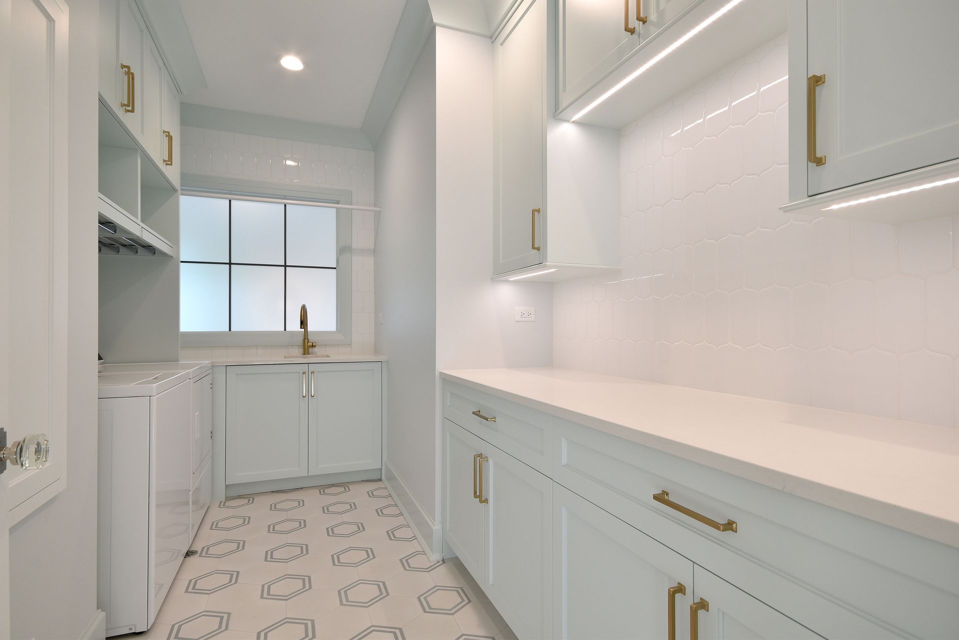 Bright white laundry room with built-in cabinets, sink, and patterned tile floor by a window.